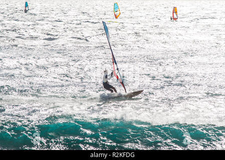 Mehrere Windsurfer in der Bucht von Medano an der Küste von Teneriffa auf einer Wasseroberfläche stark reflektierenden Sonnenlicht mit Surf Wellen. Stockfoto