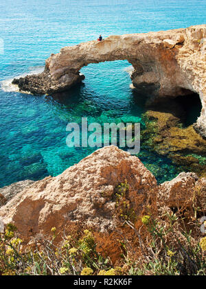 Ein Mann sitzt auf einem natürlichen Sehenswürdigkeiten Liebe Brücke. Yellow Stone Klippen in der Nähe von transparent glasklar erstaunlich grünen Wasser. Warme wolkenlosen Sommertag. Stockfoto