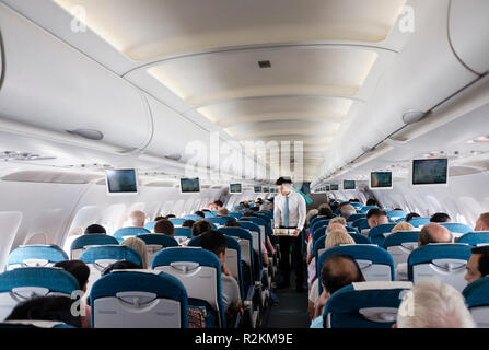 Steward, die Getränke für die Passagiere in der Economy Class Sitze in Vietnam Airlines Flug von Danang nach Ho Chi Minh Stadt. Vietnam, Asien Stockfoto