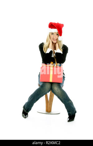 Blonde Frau mit langen Haaren und einer roten Nikolausmütze und einem Geschenk mit goldener Schleife (Weihnachten) Stockfoto