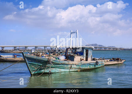 Altes, hölzernes Fischerboot mit Schrägseilbrücke auf Hintergrund, Yantai, China. Stockfoto