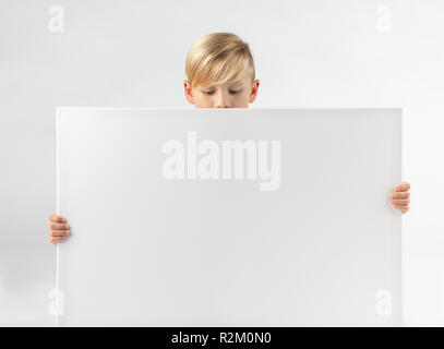 Kleine blonde Junge hält ein Schild in der Hand und sieht nach unten Stockfoto