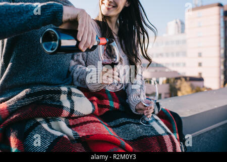 7/8 Schuß des jungen Paares in Plaid auf dem Dach und Schmollen, roter Wein in die Gläser Stockfoto