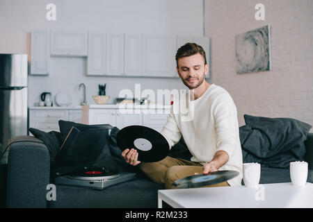 Attraktiven jungen Mann mit Scheiben auf vinyl Record Player beim Sitzen auf der Couch Stockfoto