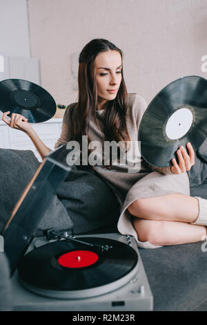 Schöne junge Frau mit Scheiben auf vinyl Plattenspieler auf der Couch zu Hause Stockfoto