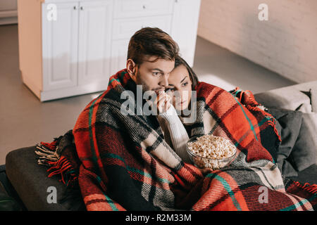 Hohe Betrachtungswinkel und der emotionalen junges Paar beobachten Film mit Popcorn auf der Couch und Abdeckung mit Plaid Stockfoto