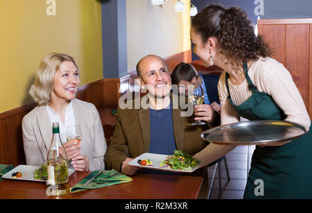 Junge Kellnerin serviert positive ältere Gäste Paar am Tisch im Restaurant Stockfoto