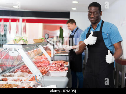 Porträt der jungen zufrieden afrikanischen amerikanischen männlichen professionellen Metzger in Metzgerei Stockfoto