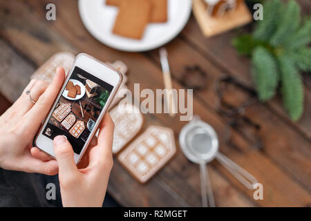 Das Mädchen macht ein Foto Flatley für soziale Netzwerke, das Ergebnis ihrer Arbeit. Bloggen, Blogger. Viel Ingwer Kekse. Weihnachtliche Stimmung, winter Morgen. Tannenzweigen und Formen zum Backen. Stockfoto