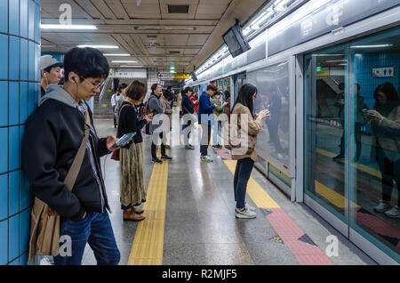 Passagiere Line up ordentlich, auf Handys spielen und für einen Zug auf der Plattform in der Samgakji U-Bahnhof in Seoul, Südkorea warten. Stockfoto