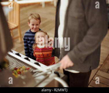 Zwei lächelnde Kinder bis auf ihren Vater, Kochen auf einen Outdoor Grill ist. Stockfoto