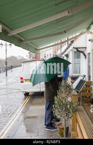 Bewdley, Großbritannien. 20. November 2018. UK Wetter: An einem Bitterkalten November Tag, mit brisk Winde und plötzliche Regengüsse, Folk sind scharf, Schutz zu suchen und zu sehen, was von dem Angebot ihrer lokalen Wirtshaus. Ein paar mit Sonnenschirm prüfen im Menü außerhalb. Quelle: Lee Hudson/Alamy leben Nachrichten Stockfoto