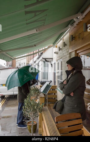 Bewdley, Großbritannien. 20. November 2018. UK Wetter: An einem Bitterkalten November Tag, mit brisk Winde und plötzliche Regengüsse, Folk sind scharf, Schutz zu suchen und zu sehen, was von dem Angebot ihrer lokalen Wirtshaus. Eine Person verlässt, wartet auf Regen zu erleichtern, während ein Paar mit Sonnenschirm prüfen im Menü außerhalb. Quelle: Lee Hudson/Alamy leben Nachrichten Stockfoto