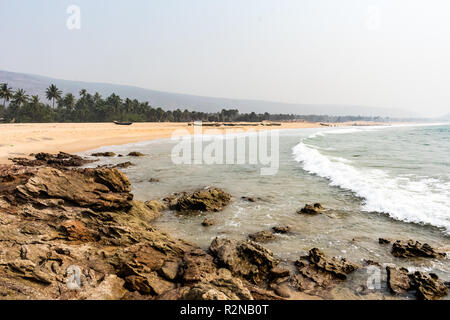 Yarada Strand mit indischen Ozeanwellen, die auf die Uferfelsen und -Steine krachen. Langzeitbelichtung mit seidig glattem Wasser und Felsen im Hintergrund. Stockfoto