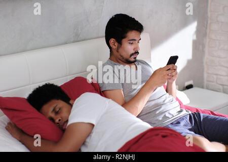 Homosexuelle Paare, Homosexuelle. Mann Fremdgehen und texting mit Liebhaber, während sein Partner im Bett schlafen ist Stockfoto