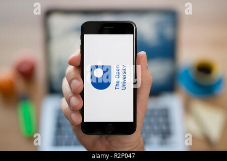 Ein Mann schaut auf seinem iPhone. Das Open Logo der Universität, während saß an seinem Computer Schreibtisch (nur redaktionelle Nutzung).