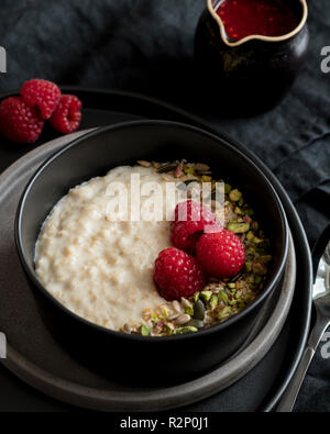 Porridge in dunklen Schale mit Nüssen und Beeren und Obst Sauce Stockfoto