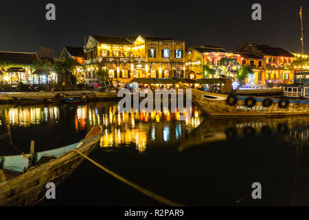 Beleuchtet, historische Altstadt von Hoi An, von den gegenüberliegenden Flußufer, Laternen auf dem Wasser spiegelt, Boote im Vordergrund. Stockfoto