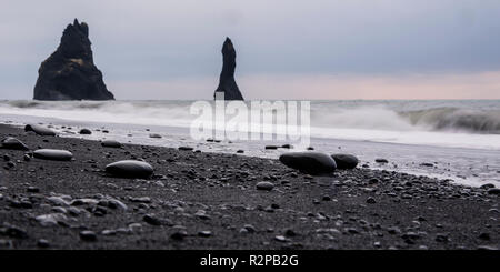 Panorama der Reynisdrangar (basaltsäulen) am schwarzen Strand Reynisfjara mit Wellen und glänzende Steine im Vordergrund. Stockfoto