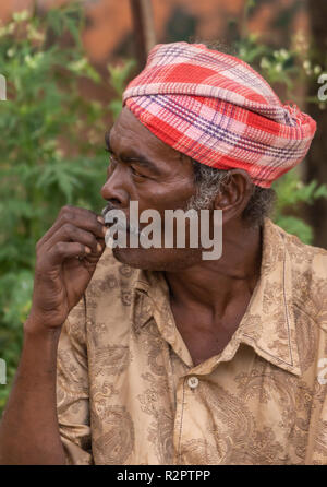 Angadihalli, Karnataka, Indien - November 2, 2013: Nahaufnahme des Gesichts des Mannes mit dem roten und weißen Turban und braunes Hemd seine Zähne Kommissionierung. Schaut weg. Gree Stockfoto