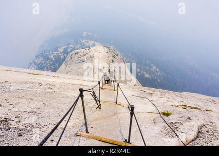 Mit Blick auf den Half Dome Kabel an einem Sommertag; Rauch, die die sub Kuppel und das Tal hinaus, Yosemite National Park, Kalifornien Stockfoto