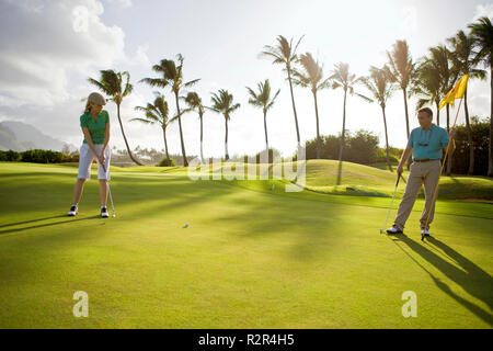 Weibliche Golfspieler Schläge als männliche Golfspieler schaut auf eine Golf Flagge. Stockfoto