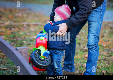 Vorschule Kind mit Vater Spaß mit Dreirad in Garten oder Park auf warmen sonnigen Tag. Aktive Freizeit mit Kindern. Stockfoto