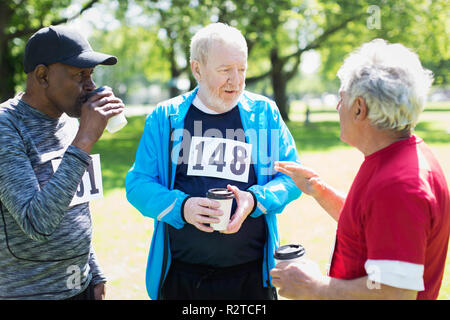 Aktive ältere Männer Freunde finishing Sport rennen und trinken Kaffee im sonnigen Park Stockfoto