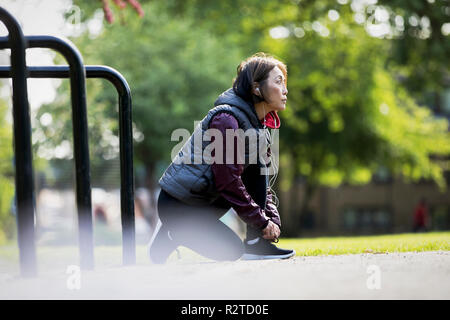 Active Senior Läuferin mit Kopfhörern Schuh binden in Park Stockfoto