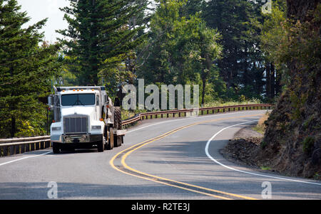 Big Rig amerikanischen Motorhaube classic Kipper Semi Truck Transport von Baumaschinen auf Schritt nach unten Auflieger und Fahrt auf der kurvenreichen Berg ro Stockfoto