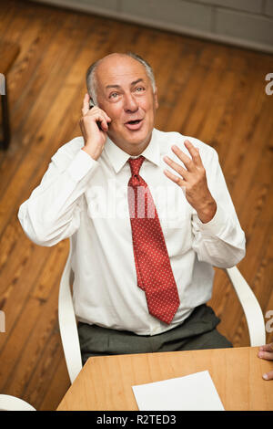 Senior Geschäftsmann am Schreibtisch sitzen, reden auf Handy. Stockfoto