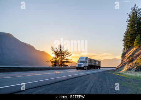 Big Rig American White Long Haul leistungsfähige Semi Truck Transport boxen mit Früchten auf Flachbett Auflieger auf geraden Abend Straße mit herrlichem Sonnen Stockfoto