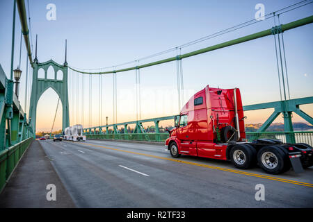 Leuchtend rote Motorhaube Big Rig Semi Truck Traktor mit Kabine, die auf dem St Johns Brücke mit einem anderen Datenverkehr über Willamette River in der industriellen Ein Stockfoto