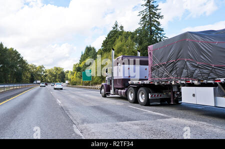 Brown Big Rig klassische amerikanische leistungsfähige Semi Truck Transport bedeckt und von Trägern der kommerziellen Ladung auf Flachbett Auflieger auf w angezogen Stockfoto