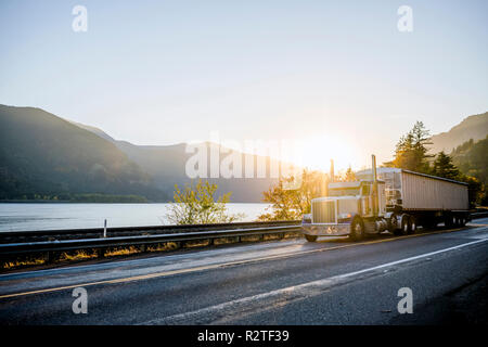 Big Rig American White Long Haul leistungsfähige Semi Truck Transport von kommerziellen Ladung in loser Schüttung Auflieger auf gerader Straße am Abend mit einem herrlichen Sonnenuntergang in Stockfoto