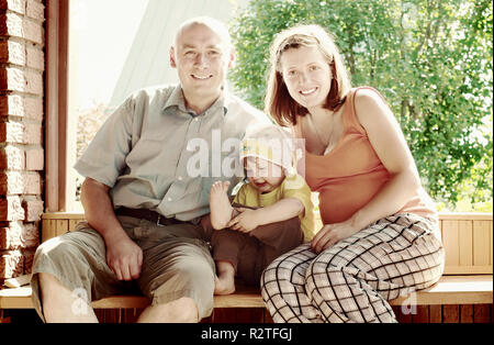 Glückliche Familie von drei sitzt auf der Bank im veranda Stockfoto