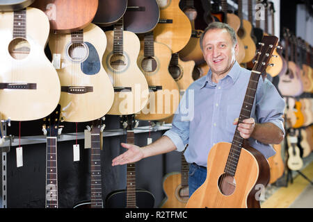 Verkäufer steht in der Nähe von akustischen Gitarren in music shop. Stockfoto