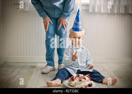 Portrait einer jungen Kleinkind sitzen mit den Überresten einer geburtstagstorte vor ihm auf einem Holzboden. Stockfoto