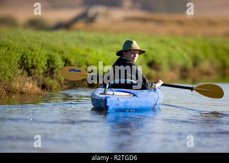 Porträt einer jungen Frau über die Schulter schauen, während der Sitzung in einem blauen Kajak an einem See. Stockfoto