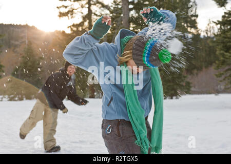 Junge Frau wird von hinten von einem Snow Ball beim Stehen in einem schneebedeckten Feld. Stockfoto