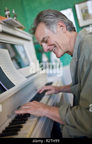 Lächelnd reifer Mann beim Spielen von Tasten auf einem Klavier. Stockfoto