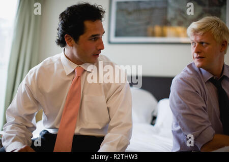 Beiden betroffenen Geschäftsleute sprechen beim Sitzen auf einem Bett in einem Hotel Zimmer. Stockfoto