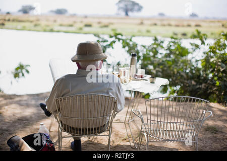 Ältere Menschen lesen auf einem Stuhl unter einem Baum an einem See. Stockfoto