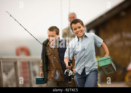 Verlassen junge Laufen hinunter einen Wharf, die Fanggeräte mit seinem Vater und seinem Bruder Stockfoto