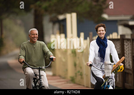 Reifer Mann und eine junge Frau, die Spaß beim Reiten Fahrräder durch eine suburban Neighborhood. Stockfoto