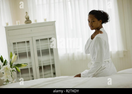 Junge Frau sitzt auf ihrem Bett tragen ein weißes Gewand. Stockfoto