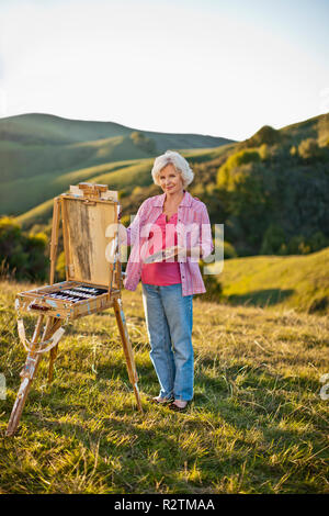 Reife Frau Malerei auf einem malerischen Hügel. Stockfoto