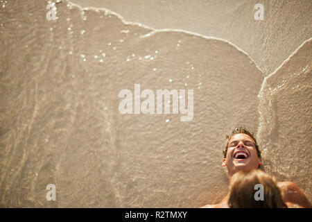 Glückliches junges Paar spielen zusammen in flachem Wasser an einem Sandstrand. Stockfoto