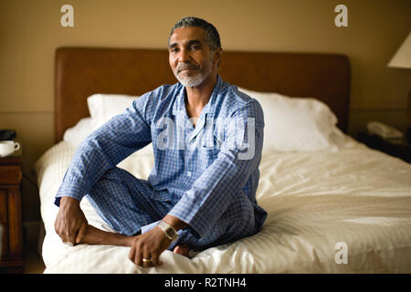 Mann sitzt im Schneidersitz auf einem Bett. Stockfoto