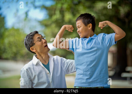 Verspielte junge flexing seine Muskeln, während sein Vater auf aussieht. Stockfoto